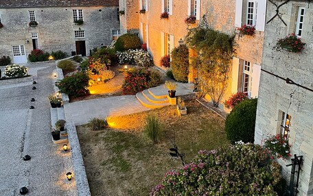 A courtyard with stone buildings, a paved walkway, and flower beds.