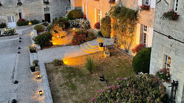 Un patio con edificios de piedra, un sendero empedrado y macetas con flores.