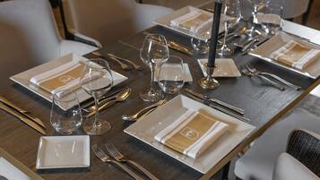 Mesa de comedor dispuesta con platos, cubiertos y copas de vino, lo que sugiere un ambiente de cena formal.
