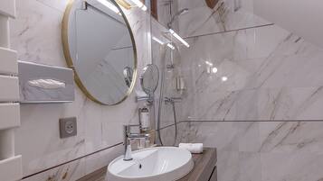 A modern bathroom with a marble wall, a wooden vanity, a round mirror, and a glass-enclosed shower.