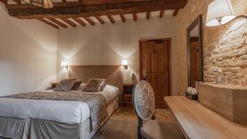 Un dormitorio con una cama, lámparas de noche, una silla de madera, una mesa y una pared de piedra.