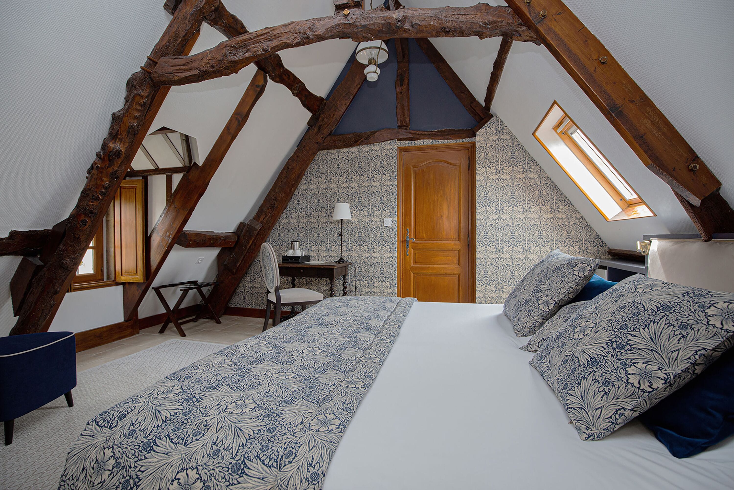 Un dormitorio con techo inclinado, una cama con ropa de cama estampada, un escritorio y una silla.