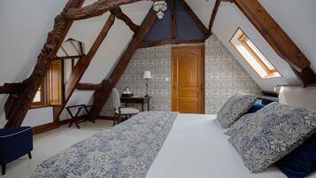 Un dormitorio con techo inclinado, una cama con ropa de cama estampada, un escritorio y una silla.