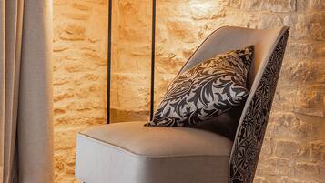 A chair with a patterned pillow in a room with a stone wall and two floor lamps.