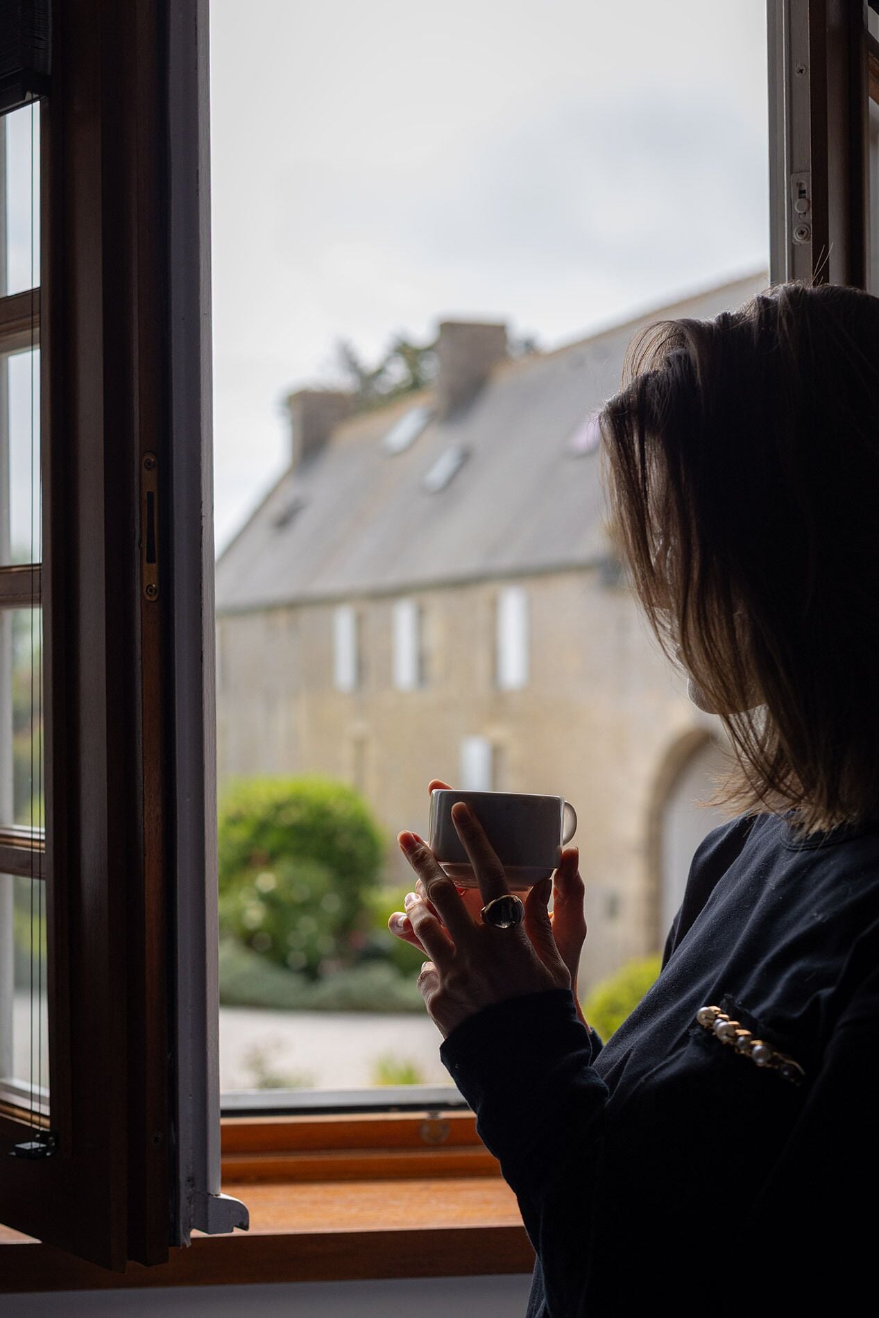 Una persona sostiene una taza junto a una ventana con vistas a un edificio.