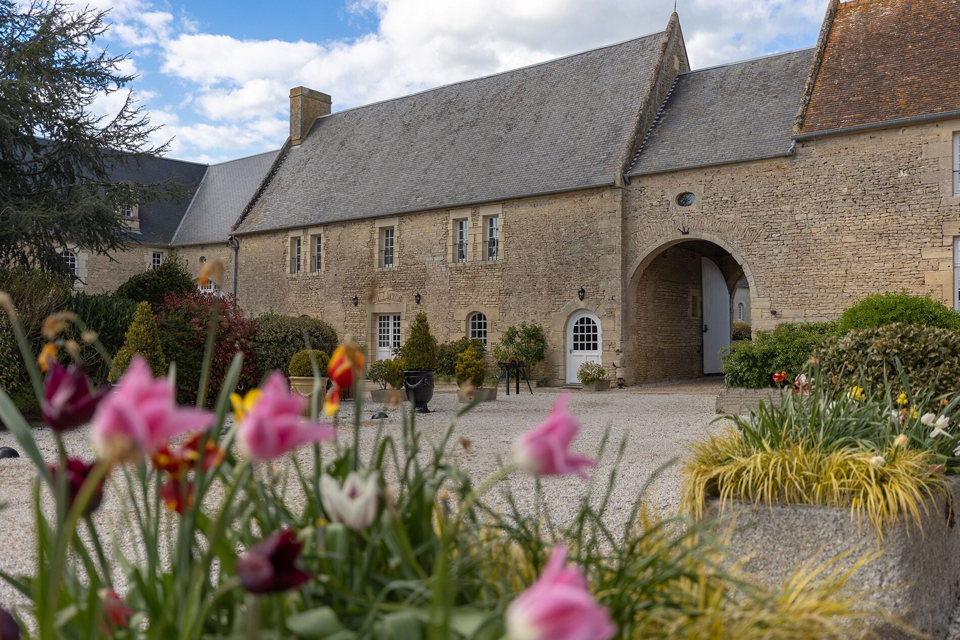 A stone building with a courtyard, featuring a large arched entrance and multiple windows.