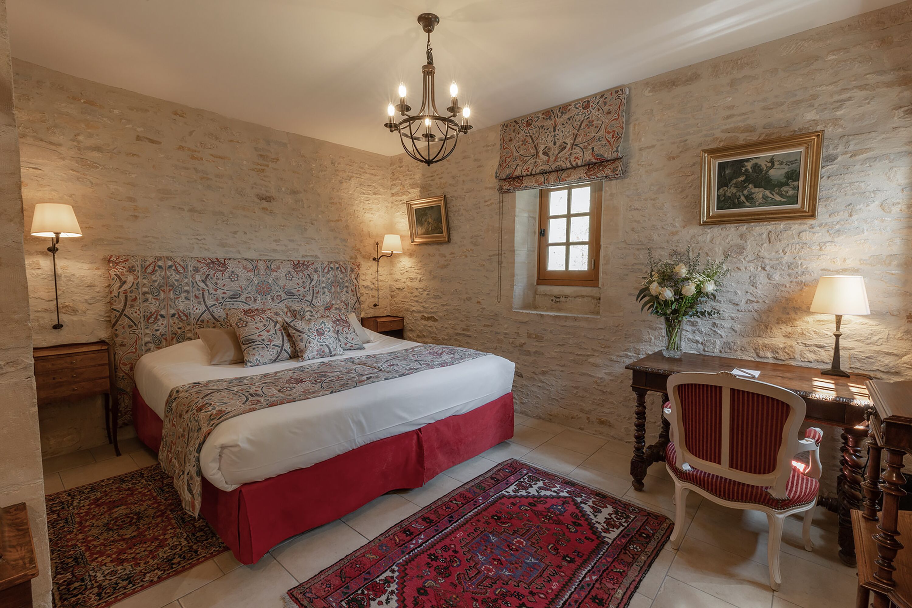 A bedroom with a large bed, a desk, a chair, and a chandelier.
