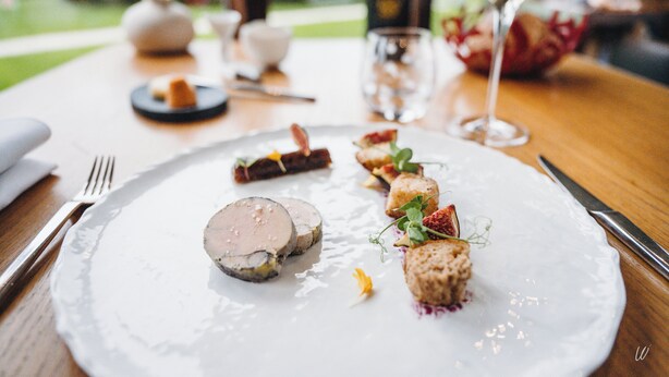 Un plato blanco con diversos alimentos, una copa de champán y un tenedor sobre una mesa de madera.