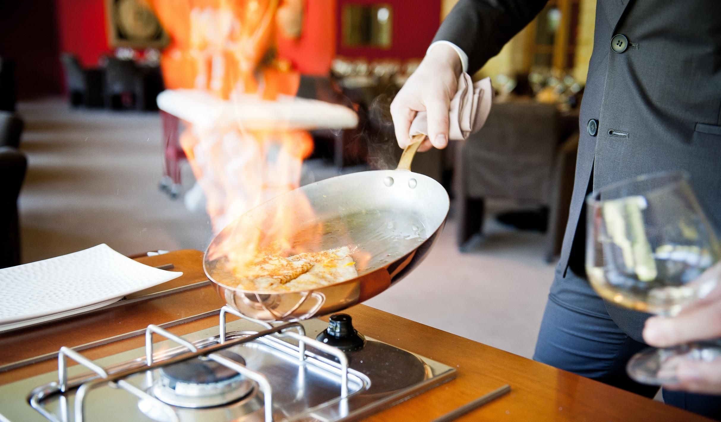 A person cooking on a portable stove with a wok, a glass of wine, and a menu on the table.