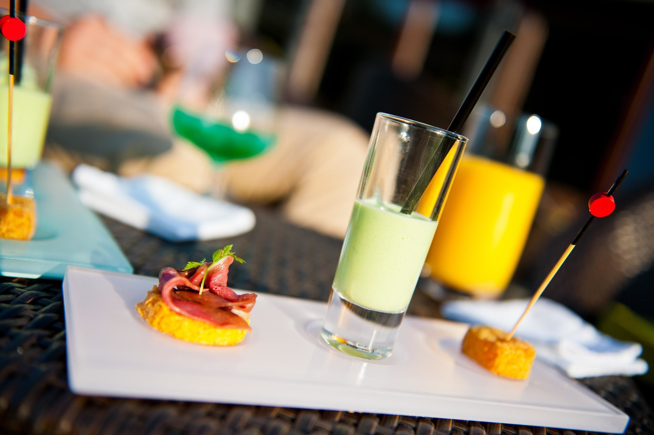 A dining table with a white plate containing a small appetizer and a glass of green beverage.