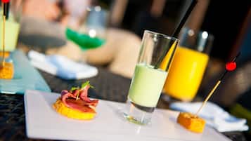 A dining table with a white plate containing a small appetizer and a glass of green beverage.