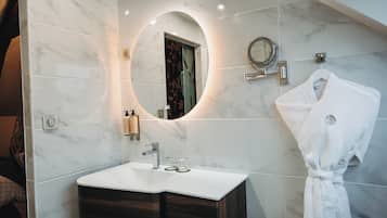 Een badkamer met een marmeren wastafelmeubel, een ronde spiegel, een badjas die aan de muur hangt, en een handdoekhouder.