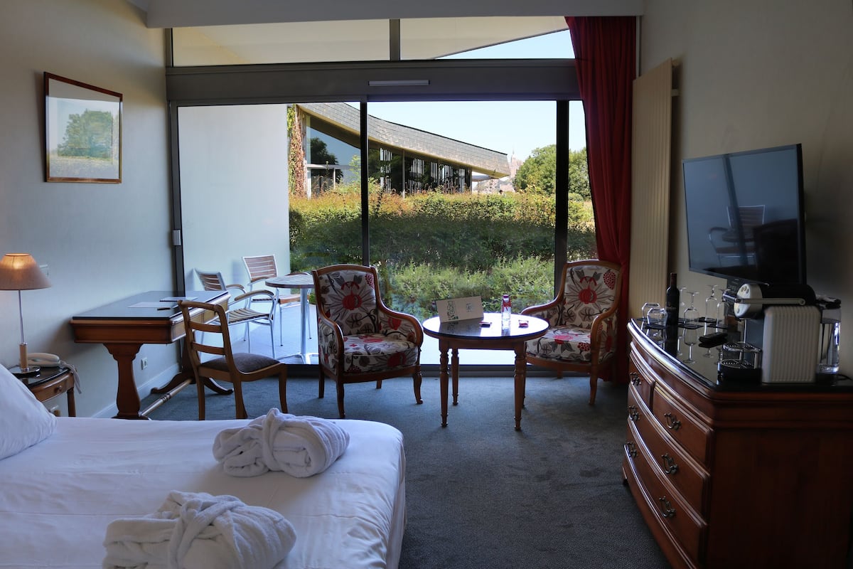 A hotel room with a bed, a desk, a chair, a table, a TV, and a view of the outdoors.