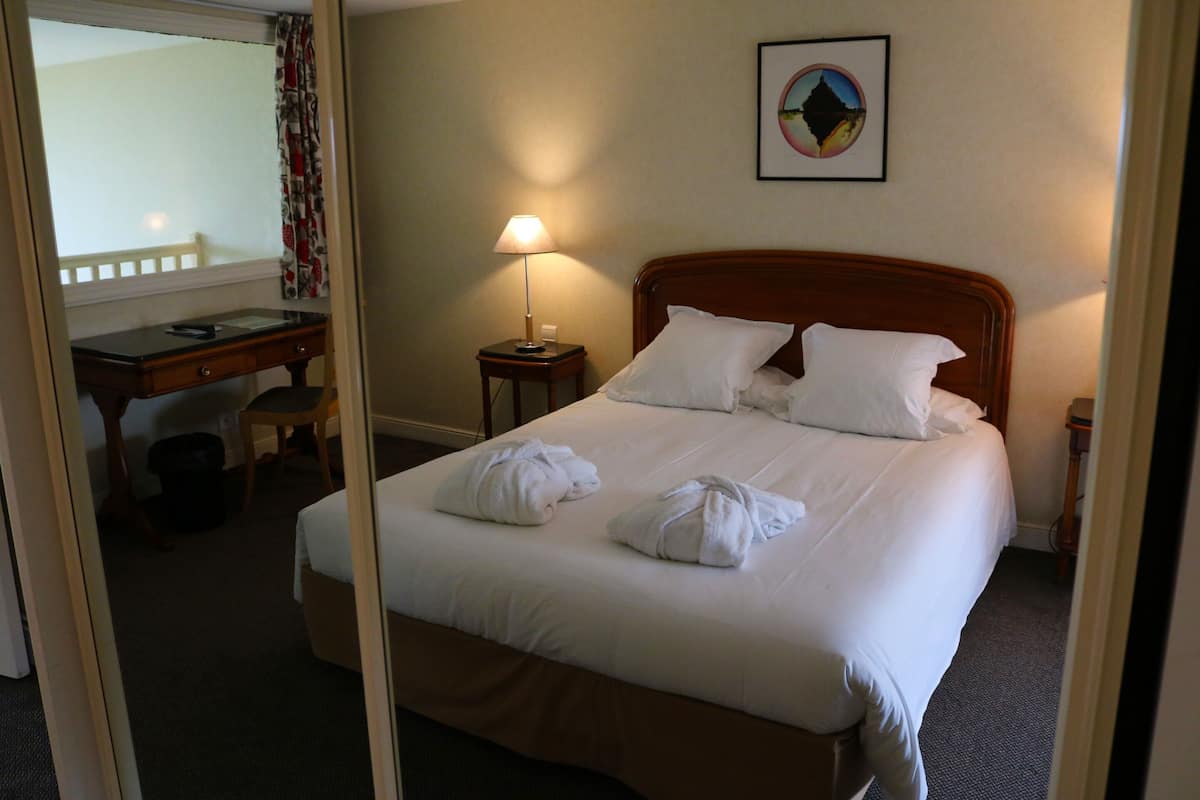 A hotel room with a bed, a desk, a chair, a lamp, and a framed picture on the wall.