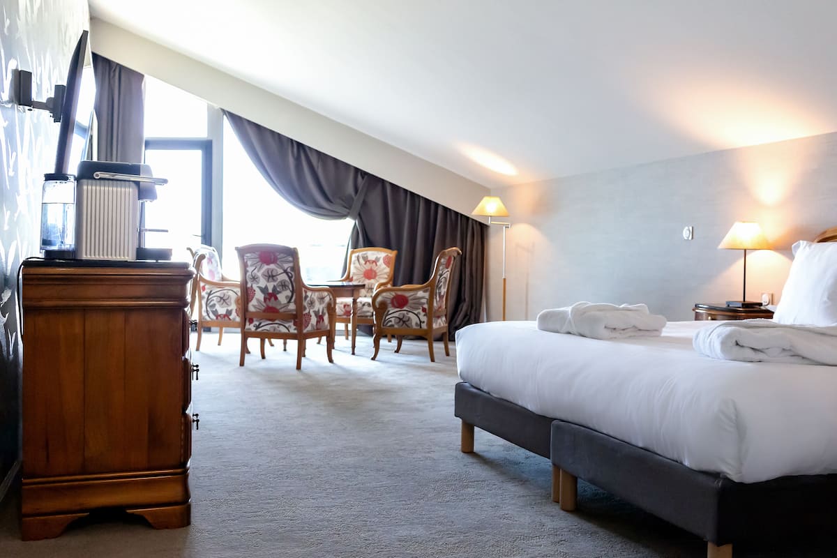 A hotel room with a bed, a wooden dresser, a desk with a lamp, and two chairs.