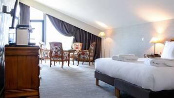 A hotel room with a bed, a wooden dresser, a desk with a lamp, and two chairs.