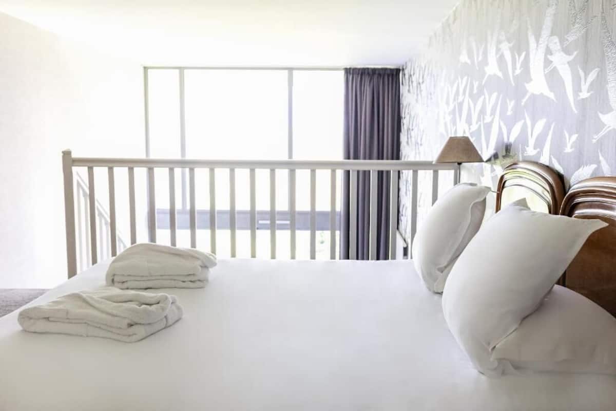 A hotel room with a balcony, white bedding, and a patterned wall.