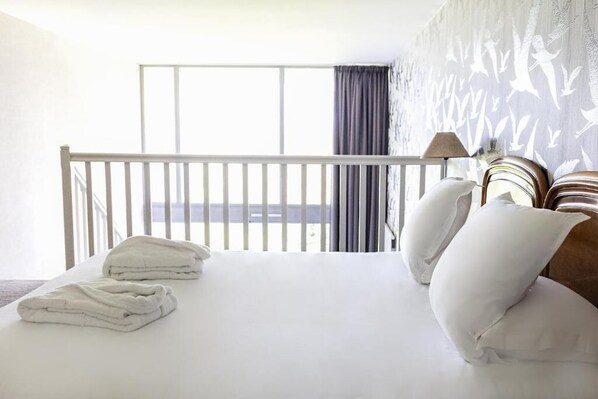 A hotel room with a balcony, white bedding, and a patterned wall.