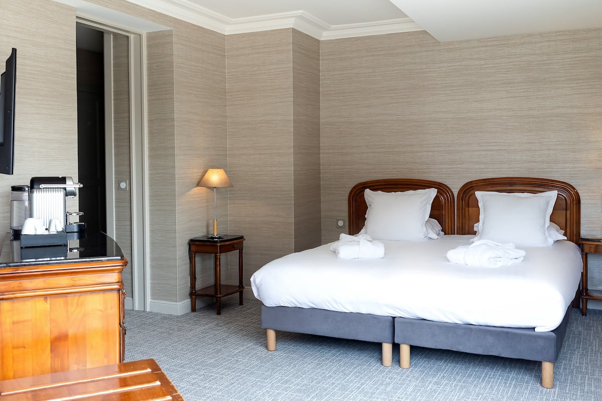 A hotel room with a large bed, a wooden dresser, a desk with a coffee maker, and a lamp.