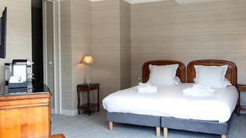 A hotel room with a large bed, a wooden dresser, a desk with a coffee maker, and a lamp.