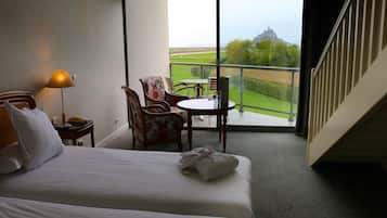 Habitación de hotel con cama, una silla, una mesa y vistas a un paisaje verde a través de amplias ventanas.