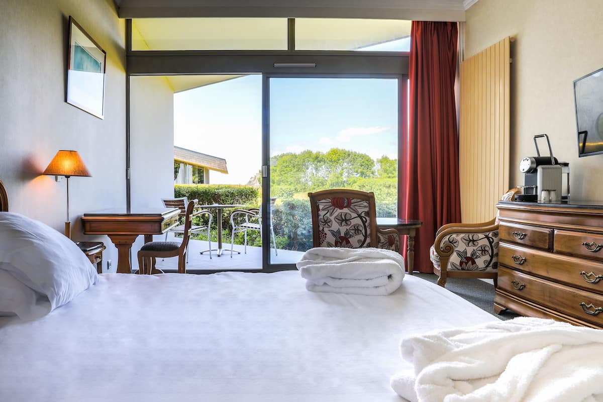 A hotel room with a bed, a desk, a chair, a dresser, and a view of the outdoors.