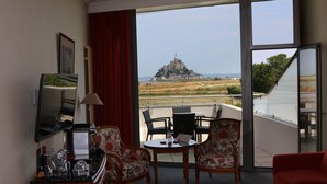A hotel room with a balcony, a table with chairs, a TV, and a desk with a lamp and toiletries.