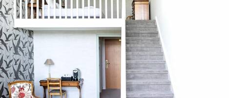 A room with a bunk bed, a desk with a lamp, a chair, and a staircase.