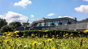 A modern building with a sign reading "RELAIS SAINT-MICHEL" in front of a lush green field with yellow flowers.