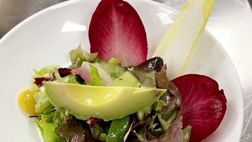 Una mesa con dos platos blancos de ensalada, cada uno decorado con hojas de rábanos y una rodaja de fruta amarilla.