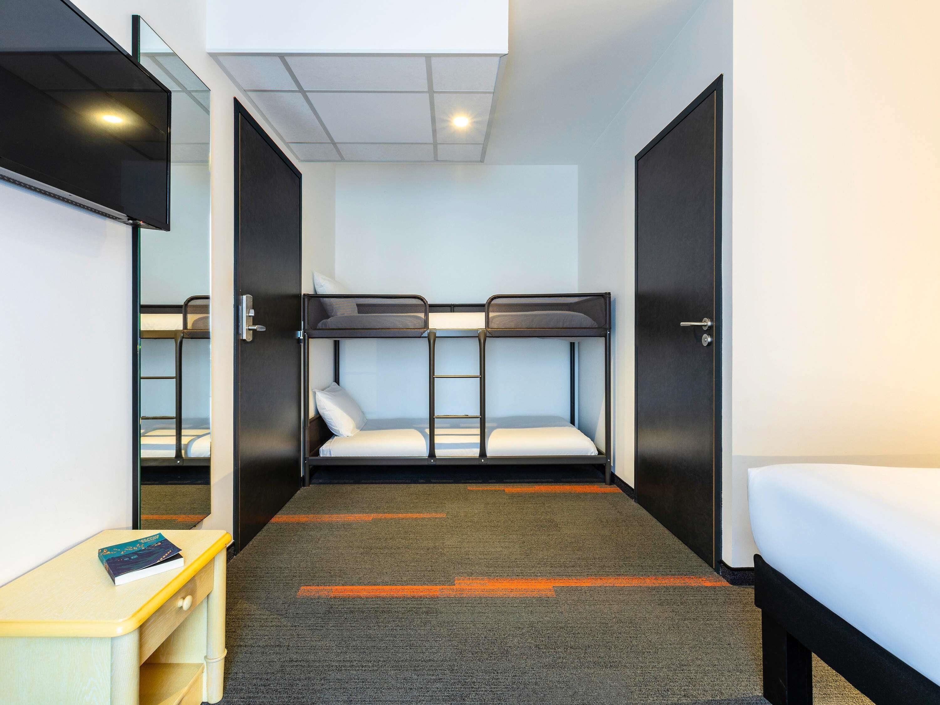 Une chambre d’hôtel compacte avec des lits superposés, un petit bureau et un miroir.