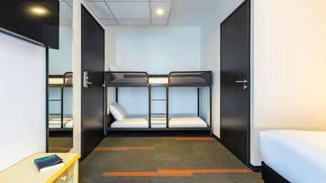 Une chambre d’hôtel compacte avec des lits superposés, un petit bureau et un miroir.
