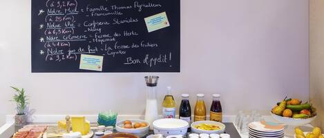 A breakfast buffet with a chalkboard menu listing local and artisanal offerings, a variety of cheeses, fruits, and beverages.