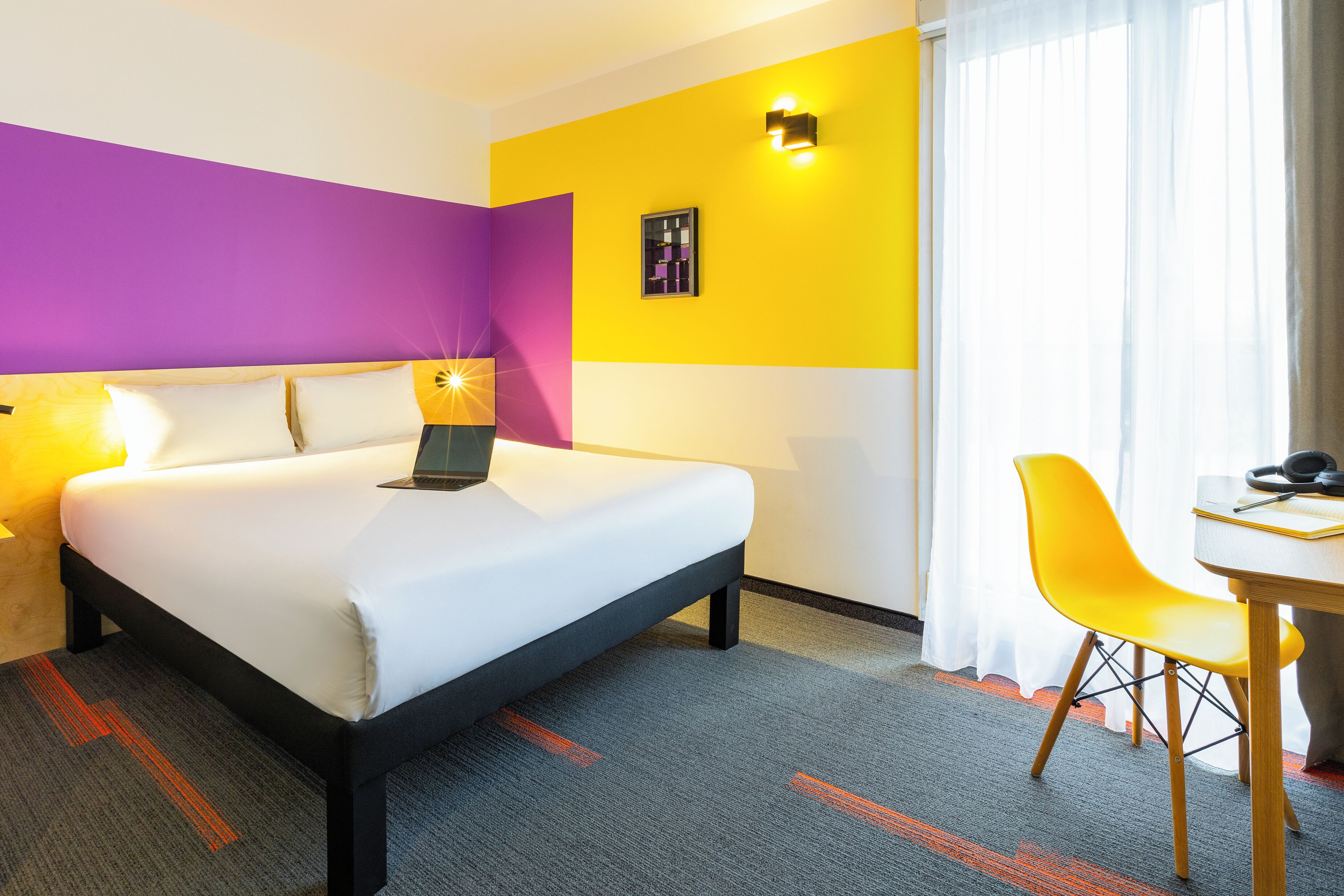 Une chambre d’hôtel avec un lit, un bureau, une chaise et une fenêtre avec des rideaux.