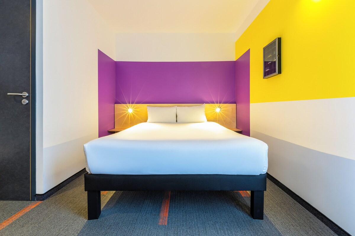 Una habitación de hotel con cama, una puerta y una pared con lámpara.