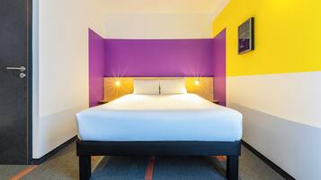 A hotel room with a bed, a door, and a wall with a light fixture.