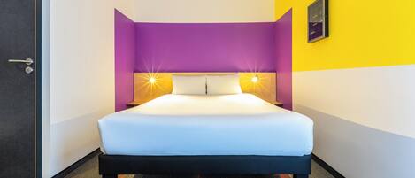 Une chambre d’hôtel avec un lit, une porte et un mur muni d’un luminaire.