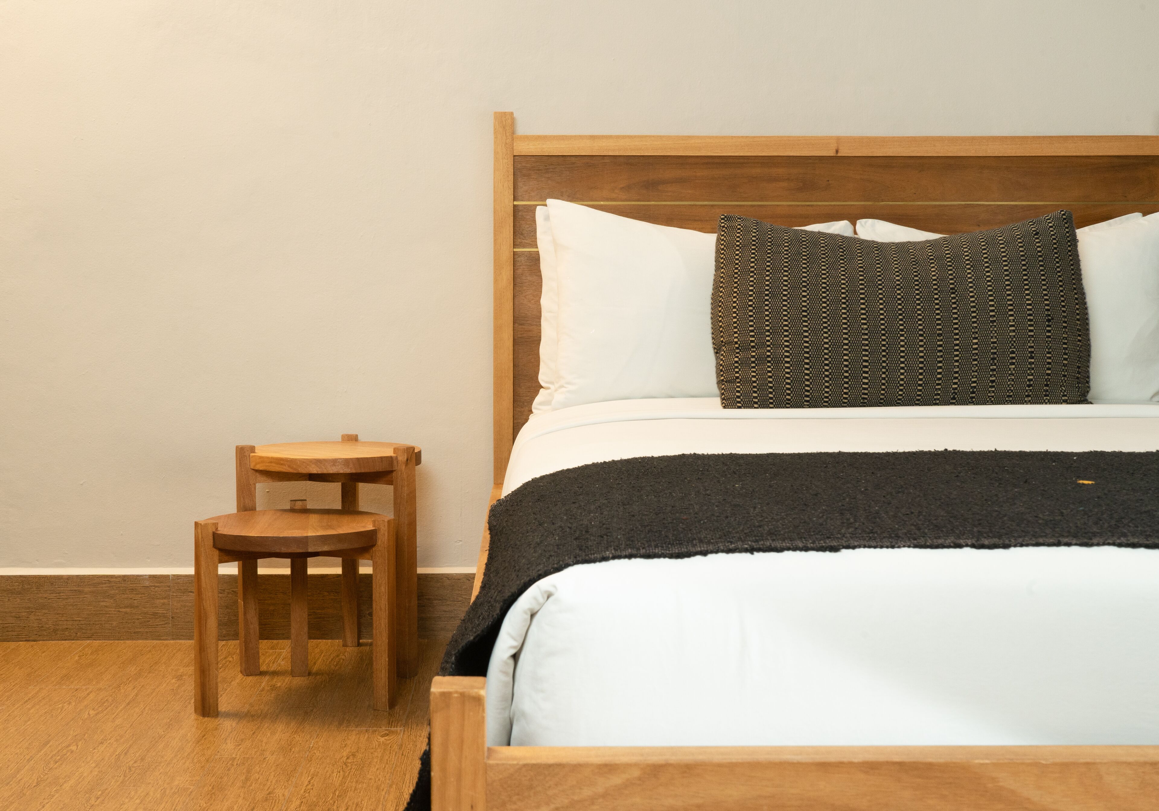 A wooden bed with white and dark pillows, a black throw blanket, and a wooden nightstand with a chair.