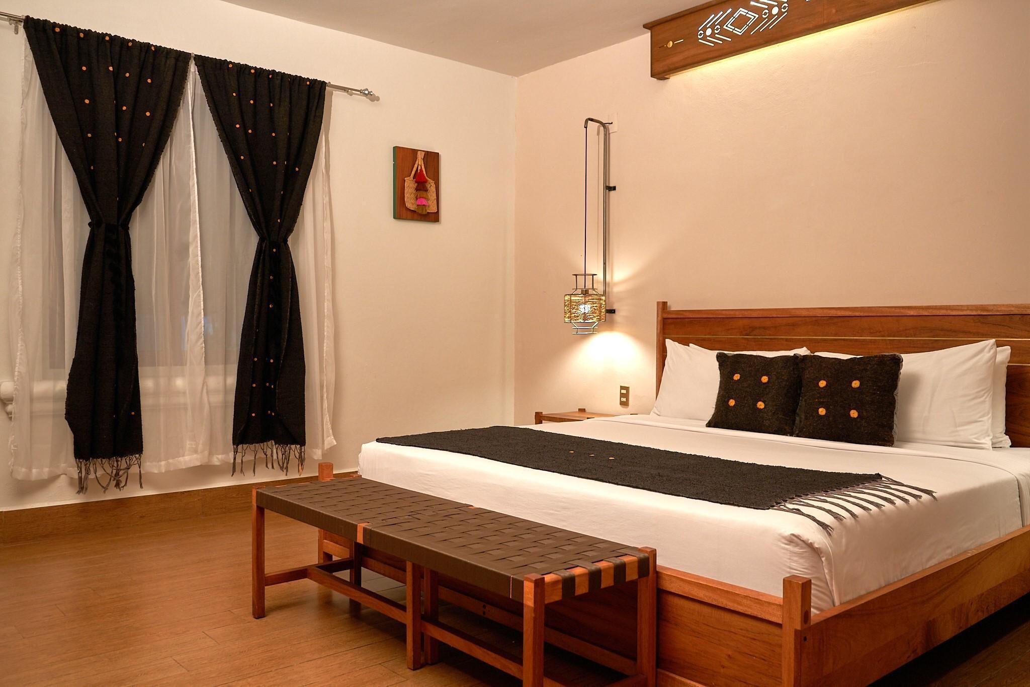 A neatly made bed with a wooden headboard, a bench at the foot of the bed, and a wall-mounted light fixture.