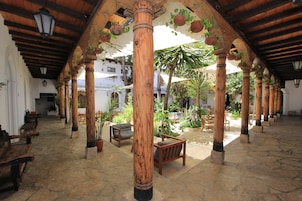Un patio cubierto con columnas de madera, suelo de piedra y mobiliario exterior.
