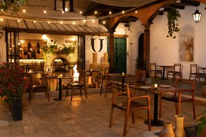 An outdoor dining area with wooden tables and chairs, string lights, and potted plants. - Hotel Sombra del Agua (San Cristóbal de las Casas)