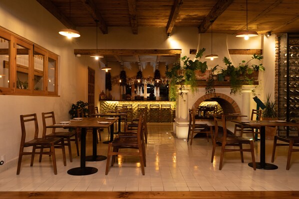 A restaurant interior with wooden tables and chairs, hanging lights, and potted plants. - Hotel Sombra del Agua (San Cristóbal de las Casas)