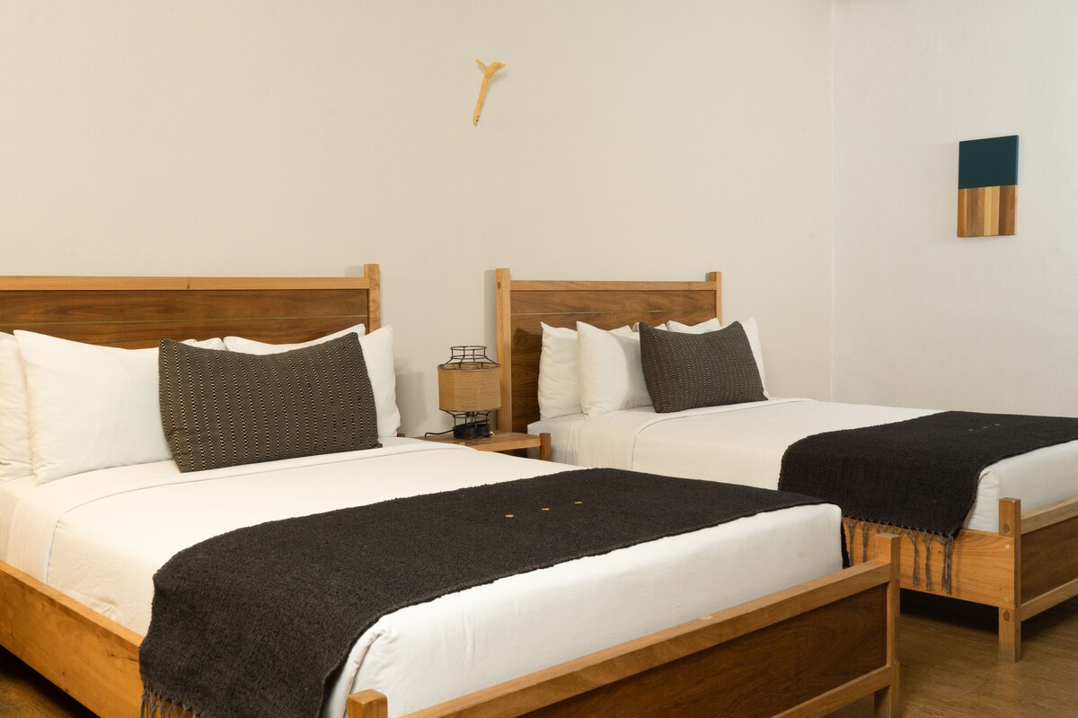 A hotel room with two wooden beds, white bedding, and a small bedside table with a lamp.