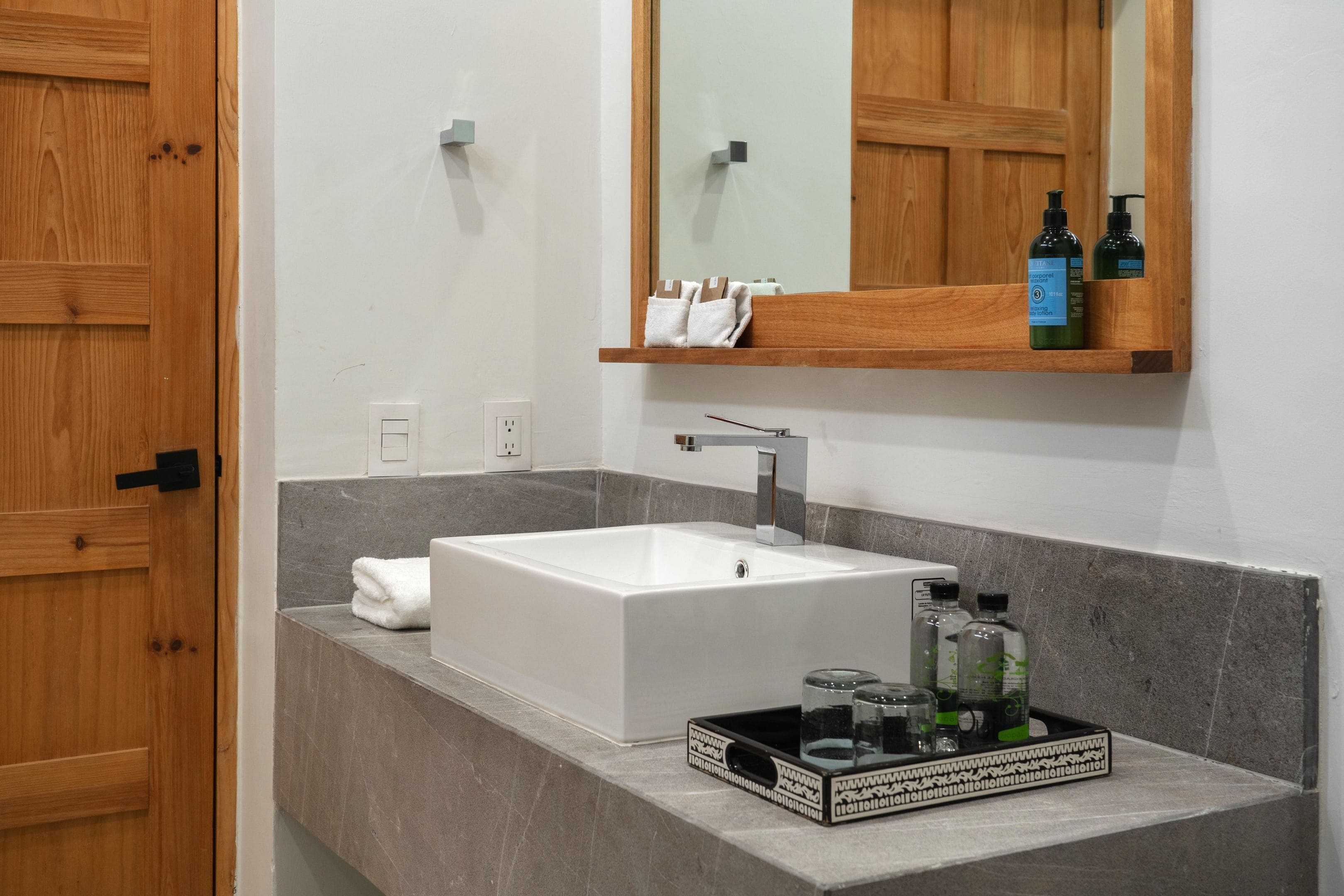 A bathroom with a white sink, wooden door, and a mirror above it. There are toiletries on the counter.