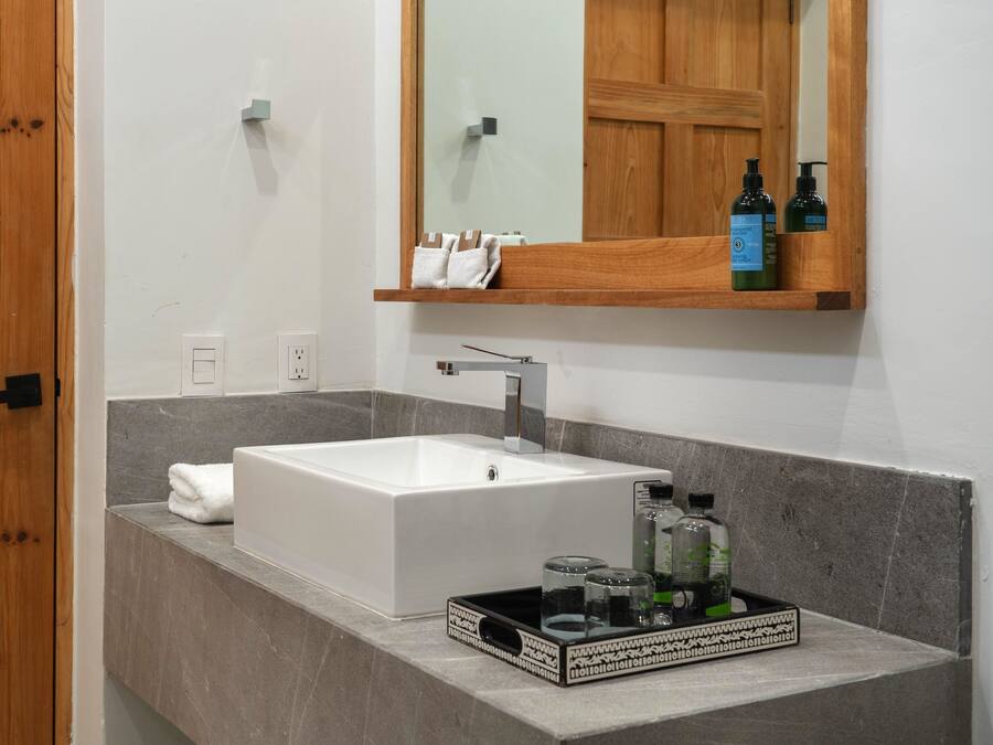 A bathroom with a white sink, wooden door, and a mirror above it. There are toiletries on the counter.