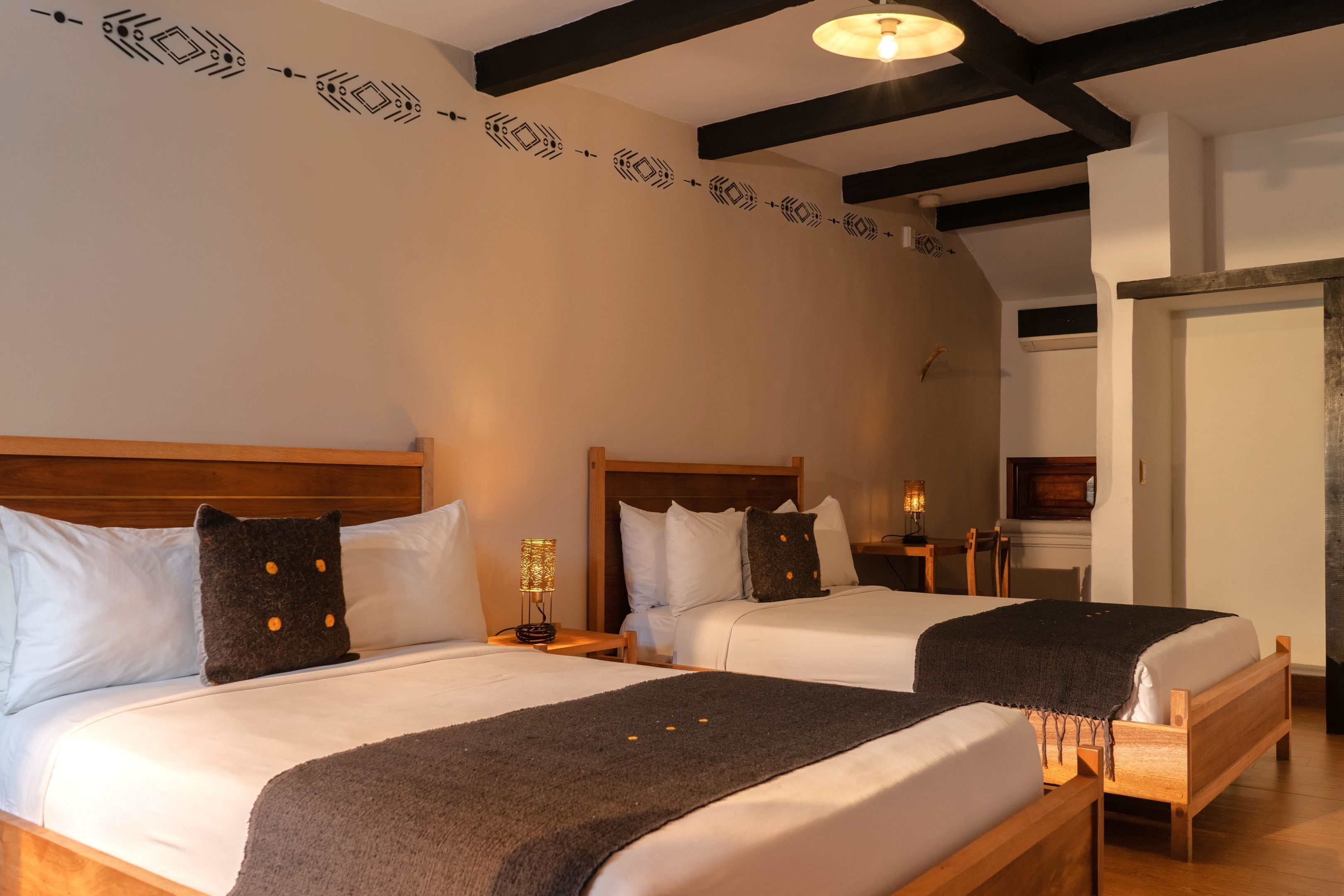 A hotel room with two beds, wooden headboards, white bedding, and a decorative wall pattern.