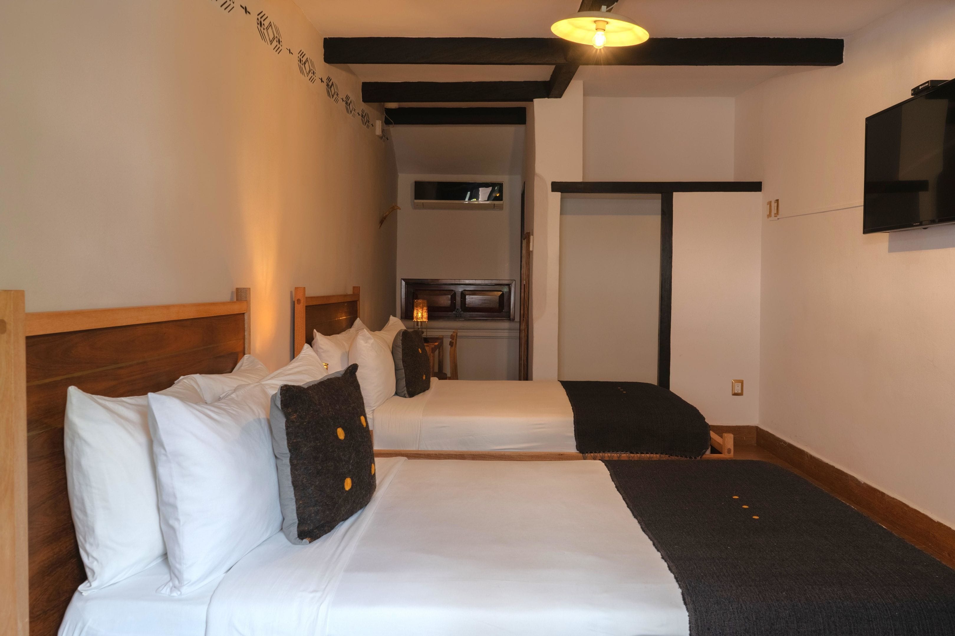 Ein Hotelzimmer mit zwei Betten, einem an der Wand montierten Fernseher und einer kleinen Küchenzeile im Hintergrund.