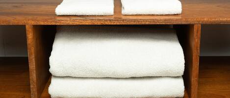 A wooden shelf with three folded white towels.