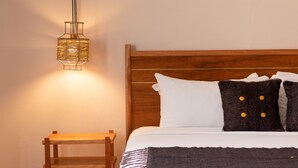 A neatly made bed with white and dark pillows, a wooden headboard, and a small wooden nightstand beside it. - Hotel Sombra del Agua (San Cristóbal de las Casas)