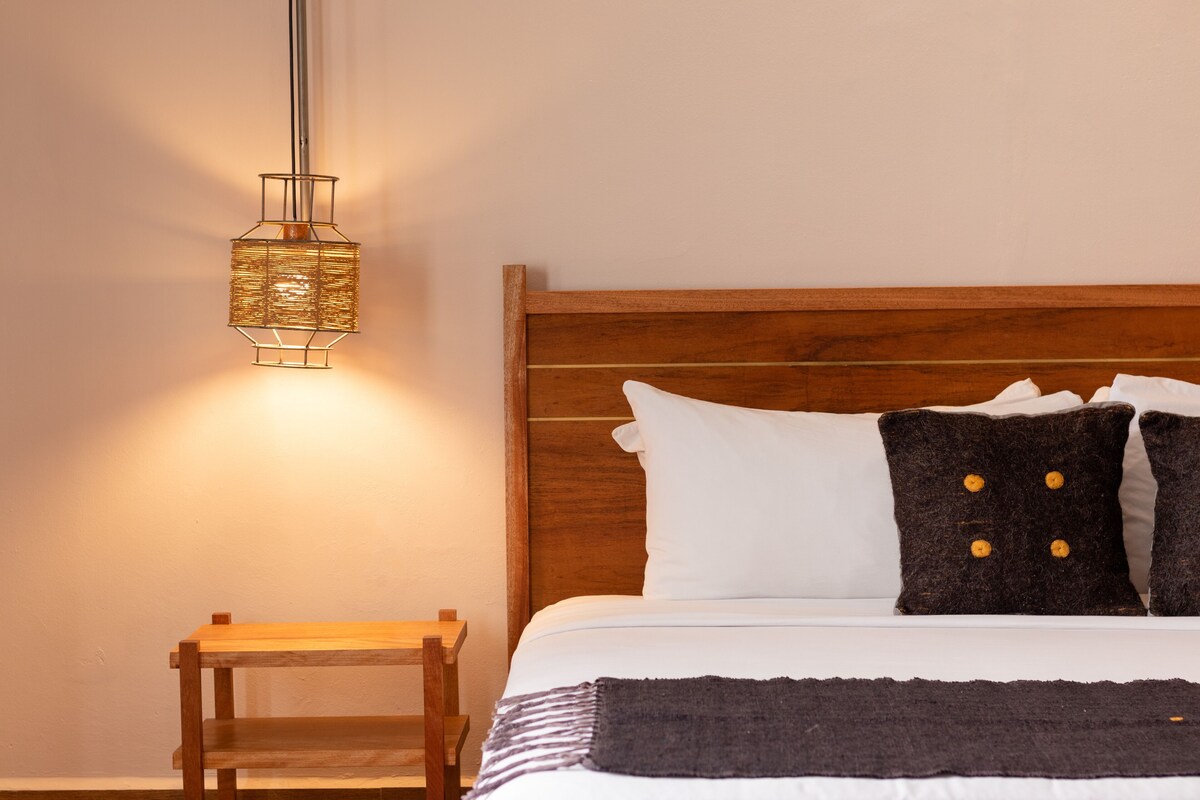 A neatly made bed with white and dark pillows, a wooden headboard, and a small wooden nightstand beside it.